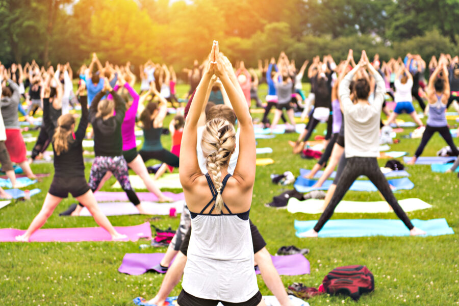 A big group of adults attending a yoga class outside in park