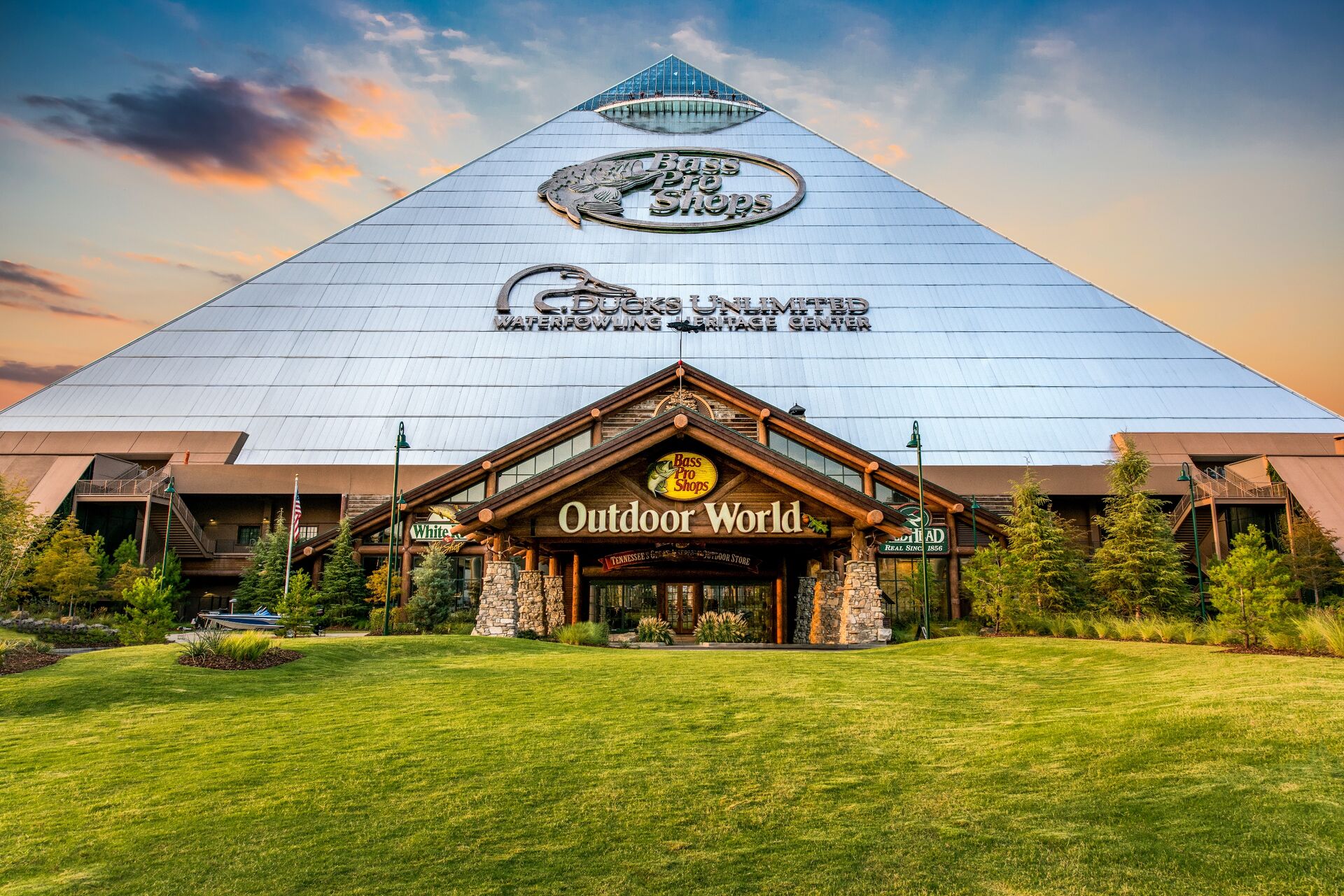 the memphis pyramid sits behind a bright green a lawn and under a sunset sky