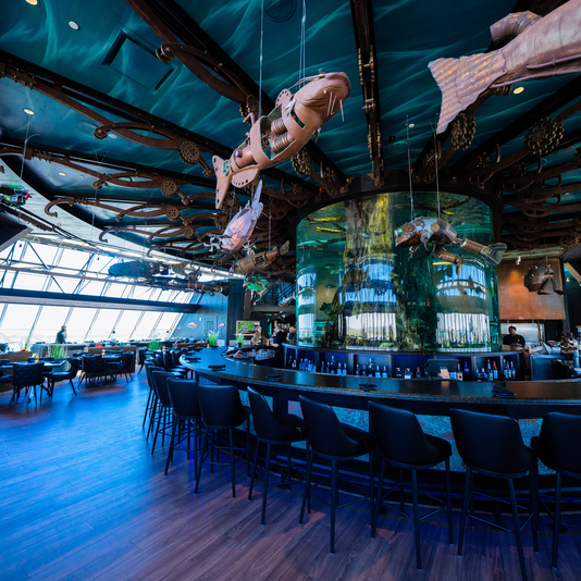 Bar that encircles a cylindrical floor to ceiling aquarium with art suspended form the ceiling that look like various Mississippi river fish made out of rusted metal